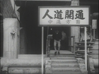 A sign over a outdoor staircase has black and grey calligraphy printed on it, in black and white cinematography.