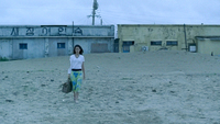 A woman walks on the beach. On the building behind her is painted a sign. The hangul, "새장여인숙" (Saejang Inn) is a play on words. Inserting space ("새장 여인 숙") converts the sign to something like "Woman in a Cage." Ironically, this indicates the position of the character.