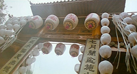 Worm's-eye view of an entryway with several lanterns hanging from it, some with red calligraphy on them. The entryway also has columns of black calligraphy on either side.
