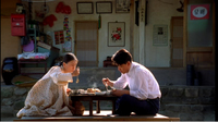 A couple sits at a table eating with banners posted on the wall with black calligraphy.