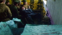 Bold calligraphy is on yellow posters in the background. Calligraphic posters are out of focus in the foreground. In the middle ground, a character is taken away by the Red Guard.