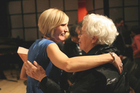 A woman with blond hair and a woman with white hair (Pauline Oliveros) face each other, smiling, each with one arm around the other in a hug.