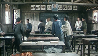 Children move around a rustic classroom, with calligraphy visible on the backwall alongside a portrait.