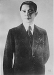 This black-­and-­white studio portrait shows Wang waist up, standing, turning slightly to the left. His shiny black hair is brushed back and his lips are tightly pressed. He looks solemn but calm, perhaps even slightly defiant. He is dressed in a dark three-­piece suit with a dotted tie. His right arm hangs down naturally, while his left arm is bent and hides behind his body. The light cast from the upper left side makes his glistening eyes and radiant face the focal point of the portrait.