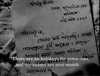 A letter is written in closeup in black Bengali by a pen entering frame at the bottom edge, about holidays and exams. It is accompanied by a white subtitle at the bottom of the frame.