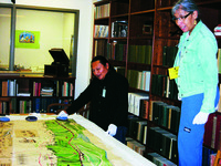 Oswaldo De Léon Kantule and Monique Mojica looking at Igwanigdibibbi’s map spread on a table.