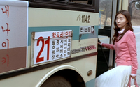A bus has red and black calligraphy and numerals printed on it. Silver English text is also afixed to it.