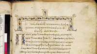 A tan parchment with Greek lettering in red, with a color bar on its left side. Ornamentation is at the top. An inscription is on the left side.