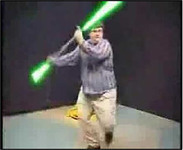 Raza in a striped shirt and khaki pants twirls a double-sided lightsaber while performing a stunt.