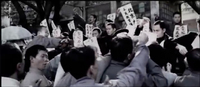 A crowd of young men is gathered holding banners with black calligraphy