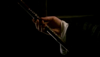 Dark image of a hand holding flute with calligraphy carved into it.