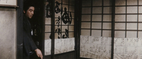 A man walks through a doorway next to black calligraphy printed on the shoji.