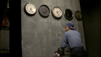 Placenames are chalked beneath a line of clocks on the wall: from left to right: Rome, LA, New York, Tokyo, Paris. The rough style and misspellings indicate the writer was poorly educated.