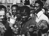 Chukwuma Ozoani stands in a crowd of people, smiling and holding a bundle of flowers.