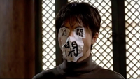 A persons face, with their eyes, mouth, and nose covered by paper and calligraphy.