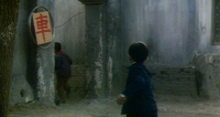 A bicycle wheel attached to a wall serves as a kind of frame for a sheet of paper with the character for "car." It is next to a door where one character departs, watched by another person close to the camera.