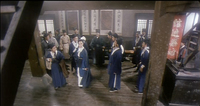 A gathering of people in blue and white clothes inside a building, with calligraphy scrolls visible on the wall in the background.