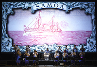 Color photograph of a police brass band playing music in front of a projected drawing of a German steamer, with the word samoa at the top.