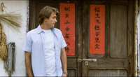 The white protagonist stands before a door adorned with a couplet written on red paper.