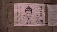 Papers posted on the wall have black calligraphy and a picture of a man's head written on them.
