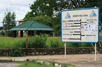 Photograph of the exterior of Luanshya mine recreation centre, behind a sign directing to sporting and recreational activities like tennis, soccer, rugby, ballroom dancing, swimming, and the former mine mess.