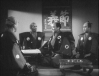 A samurai sits in the left foreground, with his back to the camera. He faces three sitting samurai in the middleground. The two samurai flanking the center samurai in the middleground are looking at and talking to the one at center. Four samurai talk before a large scroll featuring a mounted rubbing saying, _"setsugi"_ ("fidelity to one's principle; honor, humillity"). A book with calligraphic writing sits in the mid-ground.