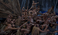 Staged photographic tableau of Polynesian voyagers crowded aboard a canoe; a man at the bow of the vessel has just sighted land.