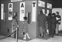 Black and white photo showing youth and adult visitors viewing a museum exhibition.