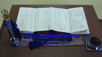 Fig. 15. A close-up photograph of Goeika bells and songbook. The handbell (rei) stands at the lower left and the flat bell (shō) sits at the lower right, with the tasseled hammer (shumoku) laying between them.