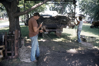 Photograph of Dean Koch mending nets while an unidentified man loads truck.