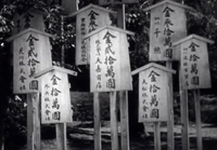 A cluster of signs on posts have black calligraphy written on them, in black and white cinematography.