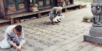 A squatting man paints calligraphy on floorboards with a white cat's tail, while another man carves the characters with a knife.