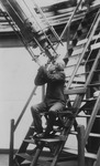 Charles Leander Doolittle sits on metal steps while looking up into a telescope.