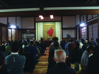 Fig. 13. A photograph of people seated on the floor of a temple room, facing away. In the background are lights and a painting.
