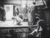 Several people gathered in a bathhouse, with calligraphy visible on signs, baskets, and noren.
