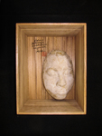 Photograph of a white plaster mask in a wooden box, with black calligraphy and red seal.