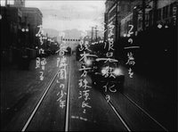 Dedication remark, in Japanese, handwritten vertically. White letters in a background scene of a busy street with cars and a tram.