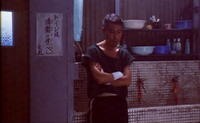 A man stands next to a banner on a wall that has red and black calligraphy printed on it.