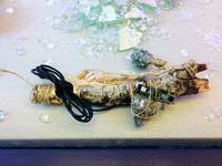 A short tree branch is wrapped in string with cowrie shells, an electronics cable linked to a small circuit board, and a resin amulet.