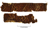 A photo of two fragments of a tapestry that features opposing bird heads in a diagonal interfacing fret. The colors are light brown, dark brown, and black.