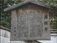 Black calligraphy on a wooden sign explaining the history of a temple in Kyoto.