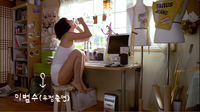 White calligraphy at the bottom left of the image of a woman drinking, perched on a stool in front of her workspace and window.