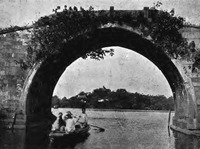A black-and-white photo of a lake scene, with a bridge taking up most of the frame. A boat, rowed by a boatman, is about to pass beneath the bridge. Two passengers on the boat are covering their faces with their hands.