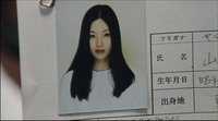 CU of a photograph clipped to a resume, with handwriting filling cells of a form on the far right edge. Resumes are usually handwritten in Japan and handwriiting is used to judge character and education.
