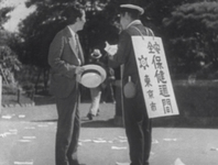 A man in suit speaks with a man wearing a sign.