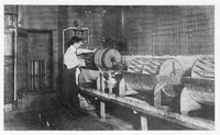 Photograph. A man wraps film onto one of three large cylinders in metal washtubs in a work room. Caption: Laboratoire de développement.