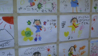 Close-up image of a wall covered in a grid of drawings made by children, all with portraits of people and calligraphy written around them.