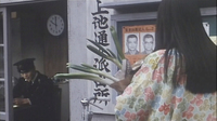 A woman carrying groceries approaches a police officer in his box. Calligraphy is visible on the sign and posters.