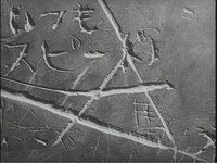 White calligraphy is carved into stone, in black and white cinematography.