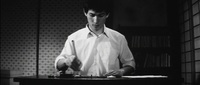 A man sits at a table brushing calligraphy, in black and white cinematography.